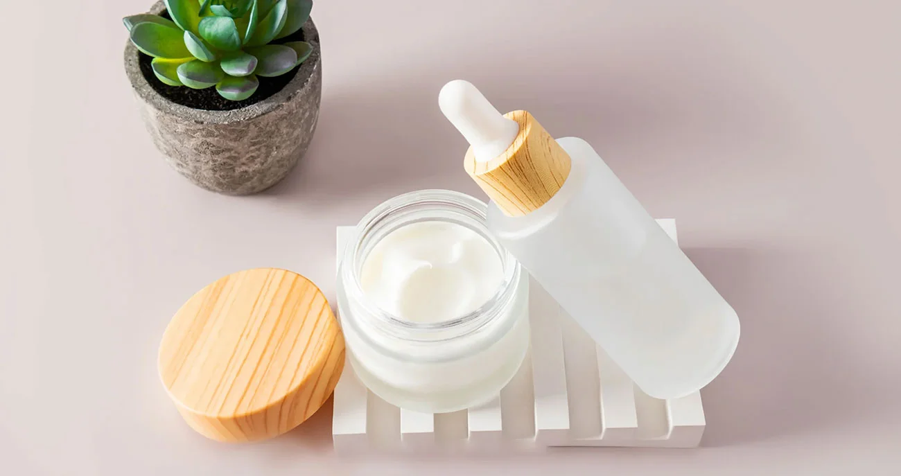 Jars of skincare items with wooden lids next to a succulent plant on a light background.